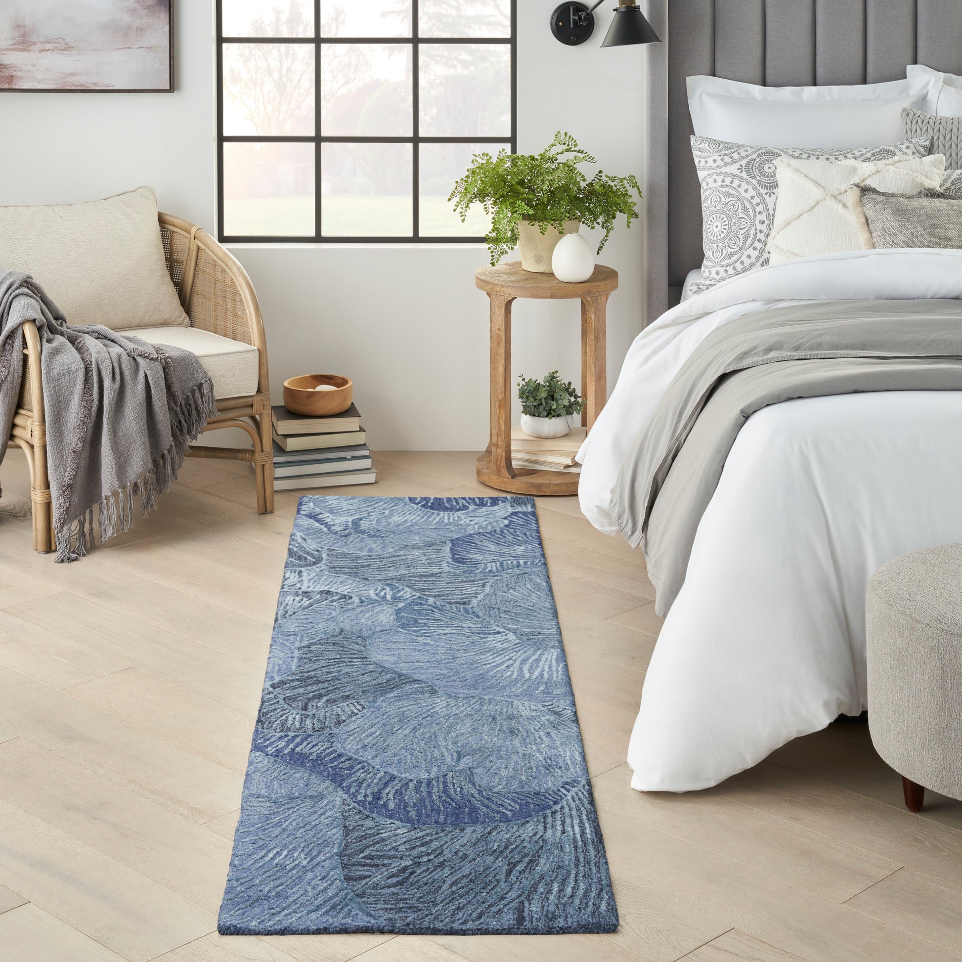Blue botanical patterned runner rug in a bright bedroom beside a bed, wicker chair and wooden side table.