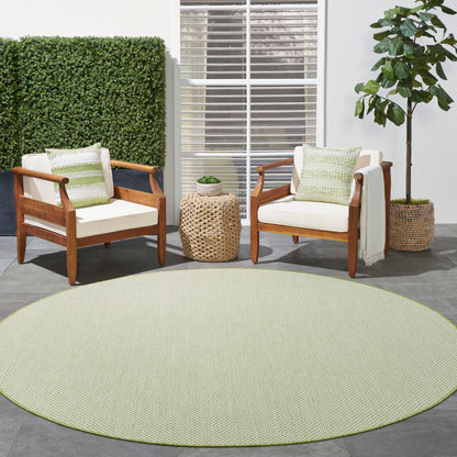 Two wooden armchairs with cream cushions and green pillows, round pale-green rug, woven rattan side table, potted plant.
