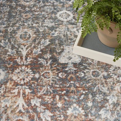 Rust, blue, and ivory floral patterned rug with vintage vibe; potted fern on a light tray rests on it.