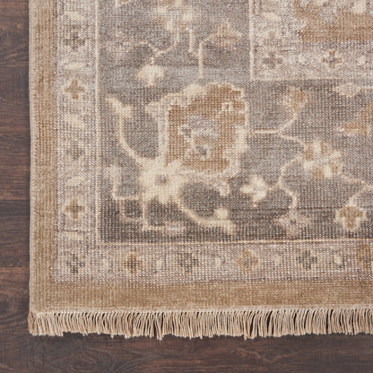 Neutral woven area rug with floral border & fringe, taupe, cream & beige tones on dark wooden floor.