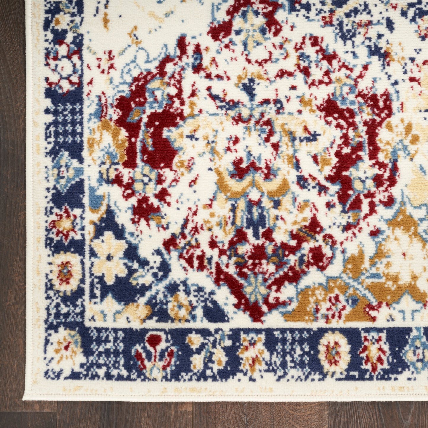 Traditional oriental rug with cream field, red, navy and gold floral pattern, navy border and ivory fringe on wood floor.