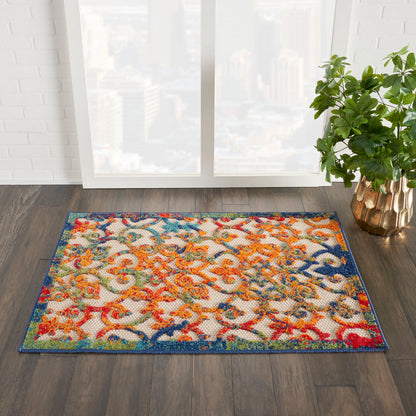 Rectangular woven area rug with a vibrant multicolor floral/scroll pattern and blue border on dark wood floor beside a green potted plant.