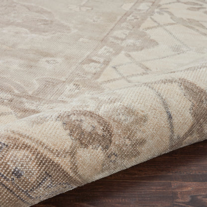 Beige woven rug with faded geometric pattern, folded corner on dark wood floor, neutral vintage style.