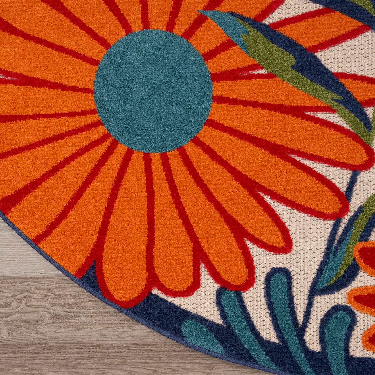 Bold tropical floral round rug with large orange petals & teal center, blue border, woven texture on wood floor.