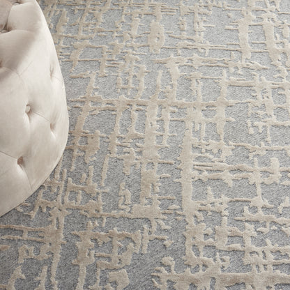 Beige tufted ottoman beside a gray-blue abstract patterned rug.