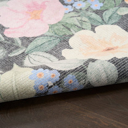 Floral printed woven fabric with large pink & cream flowers, blue blossoms, green leaves, folded edge on dark wood surface.