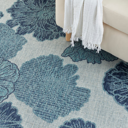 Blue and teal floral patterned area rug with large petals under a beige sofa and a white fringed throw.