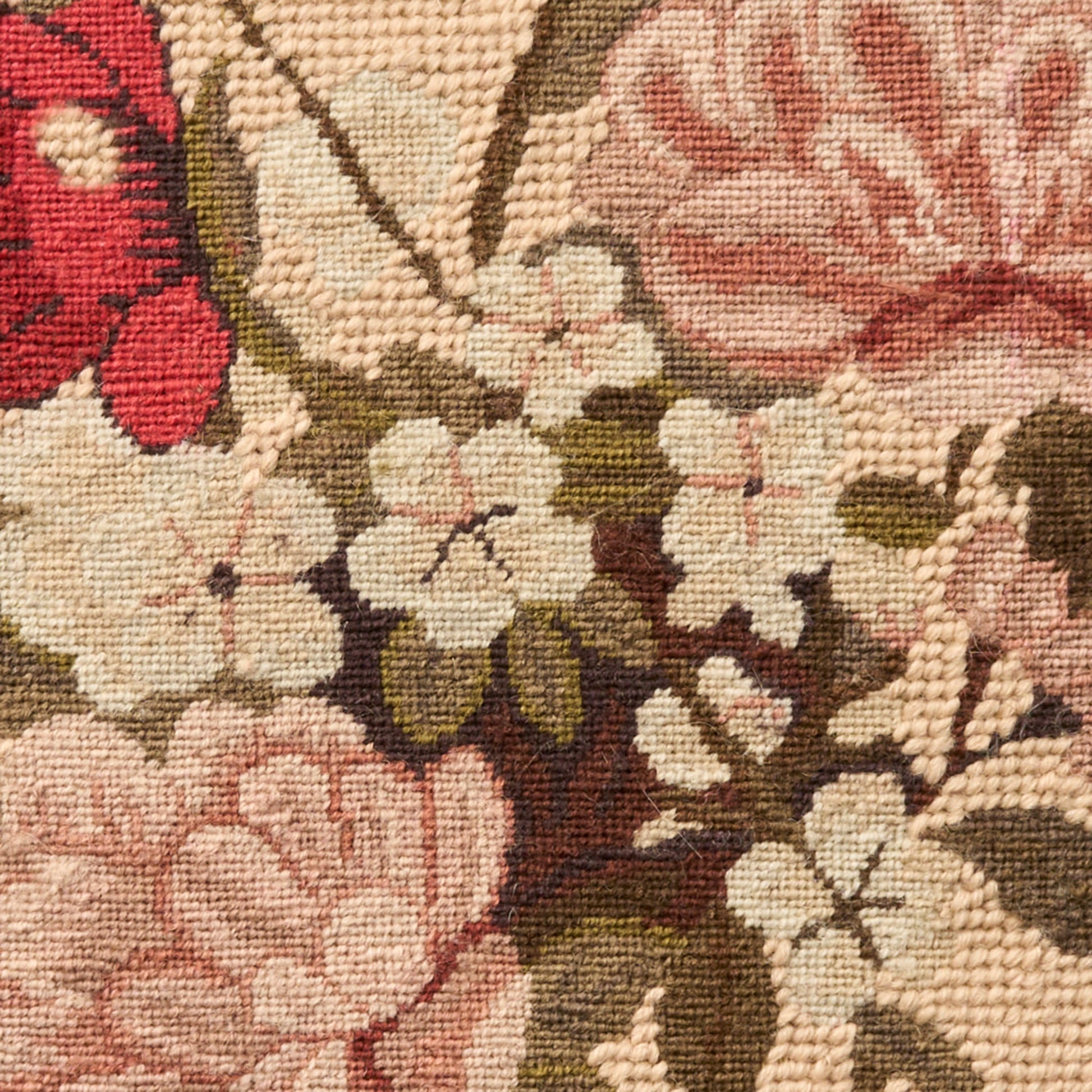 Close-up of a floral tapestry rug with pink, cream, and red blossoms and brown stems on a warm beige background.