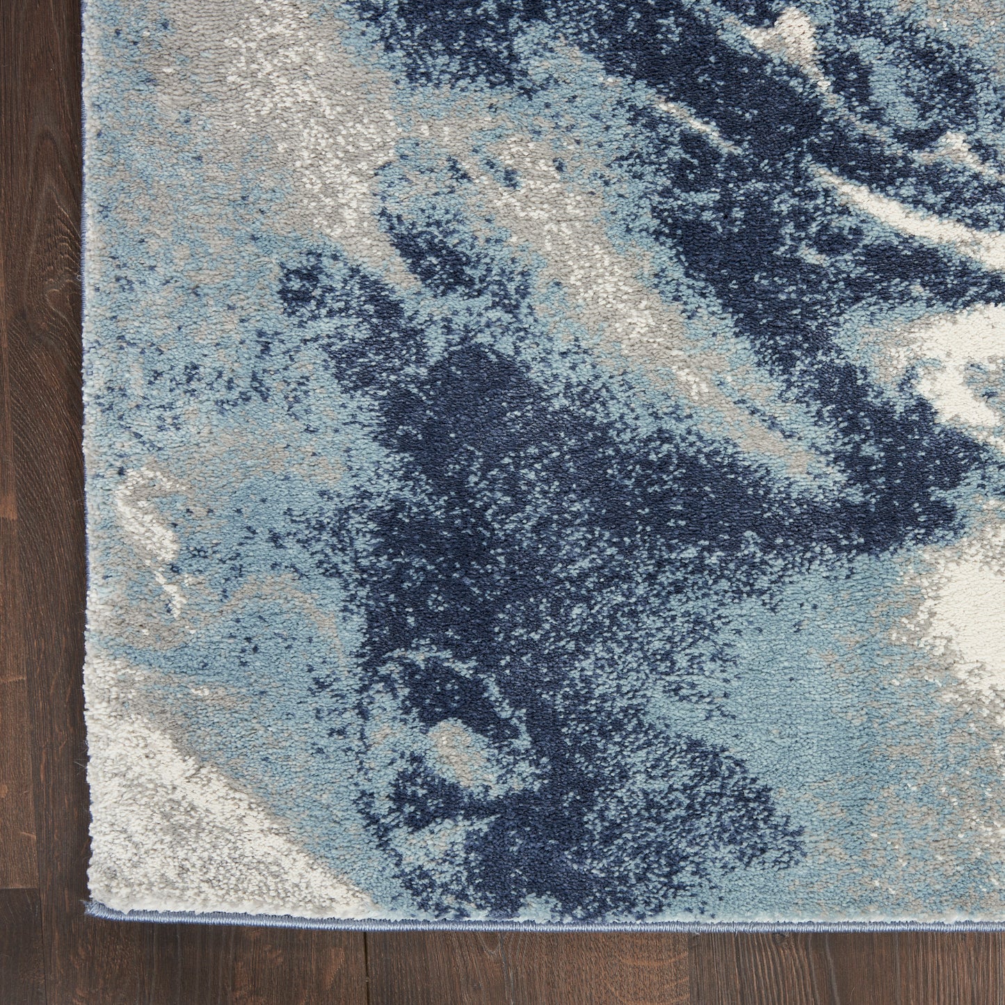 Abstract blue area rug with navy, sky blue, and white patches on a dark wood floor.