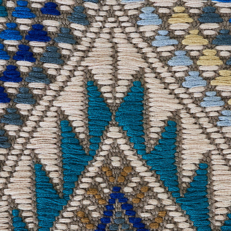 Close-up of a woven kilim rug with geometric diamonds and chevrons in teal, cream, tan, and brown.