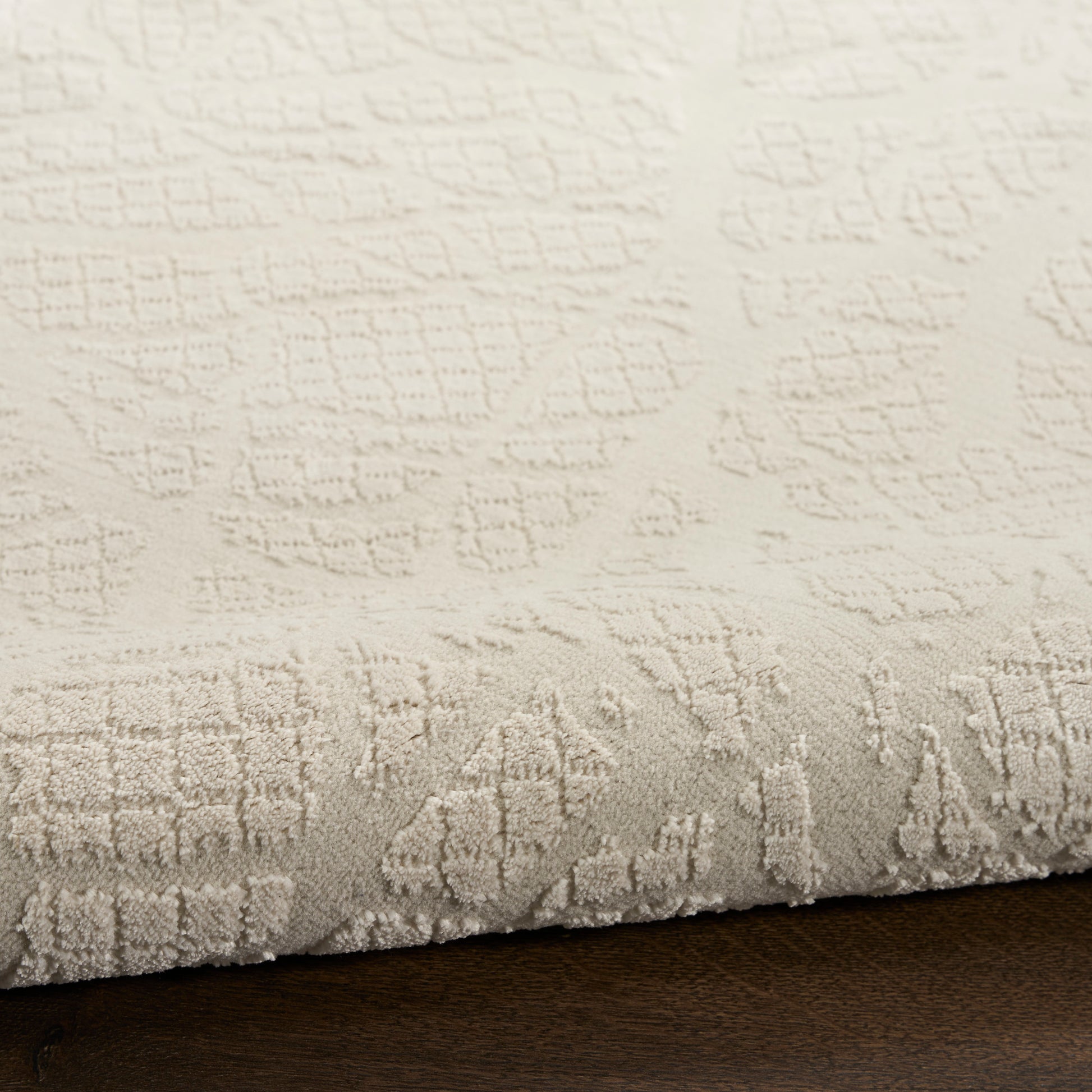 Cream textured area rug with subtle raised geometric pattern, plush pile on dark wood floor.