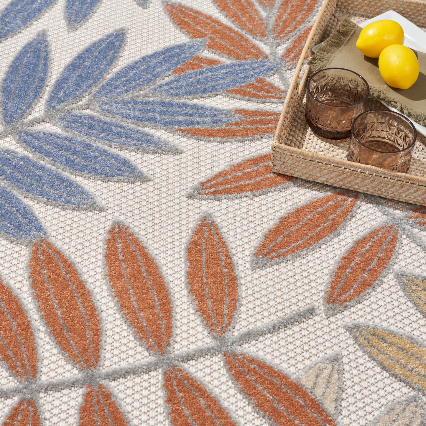 Outdoor woven rug with blue and orange leaf motifs on beige