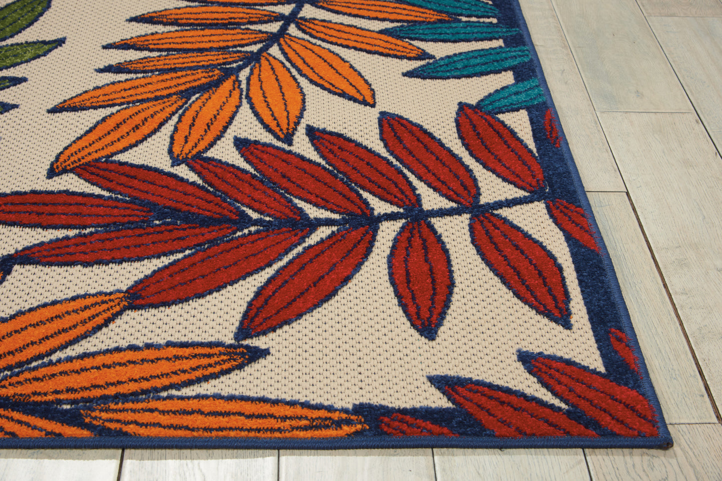 Beige textured woven rug with orange, red and teal leaf pattern and navy border on tiled floor.