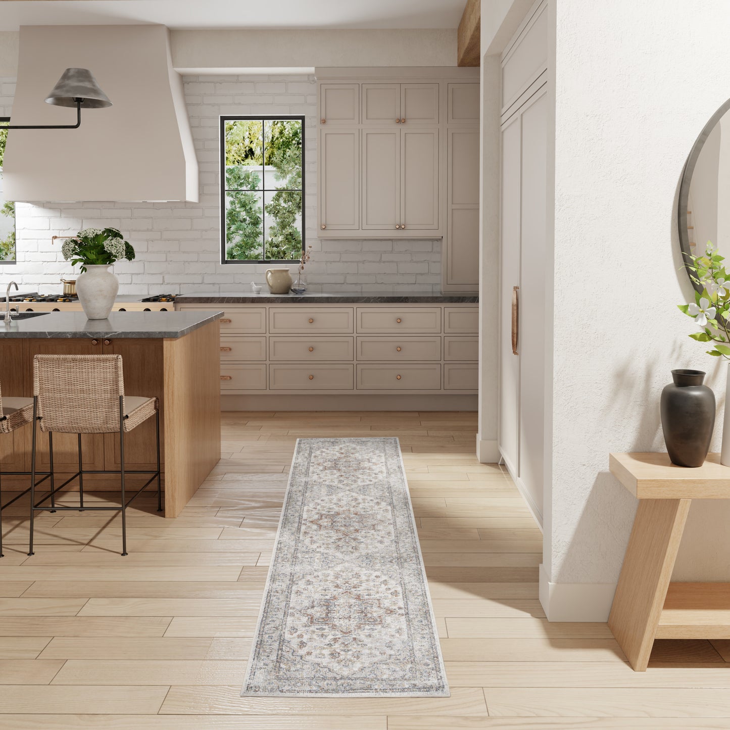 Bright kitchen with cream cabinets, gray countertops, wooden island, woven stools, patterned runner rug, and wall mirror.