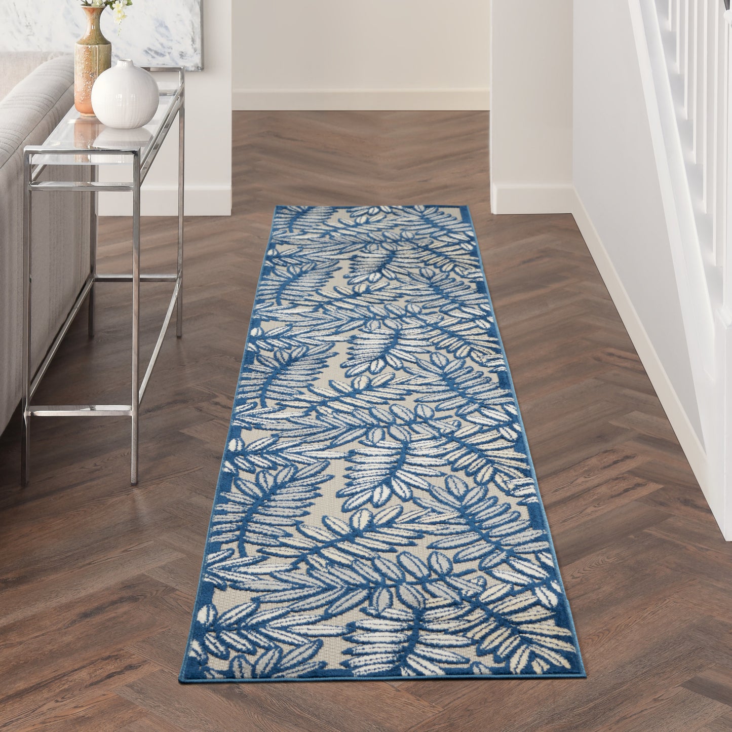 Beige runner rug with blue leafy pattern and blue border in a dark-wood hallway beside a glass console.