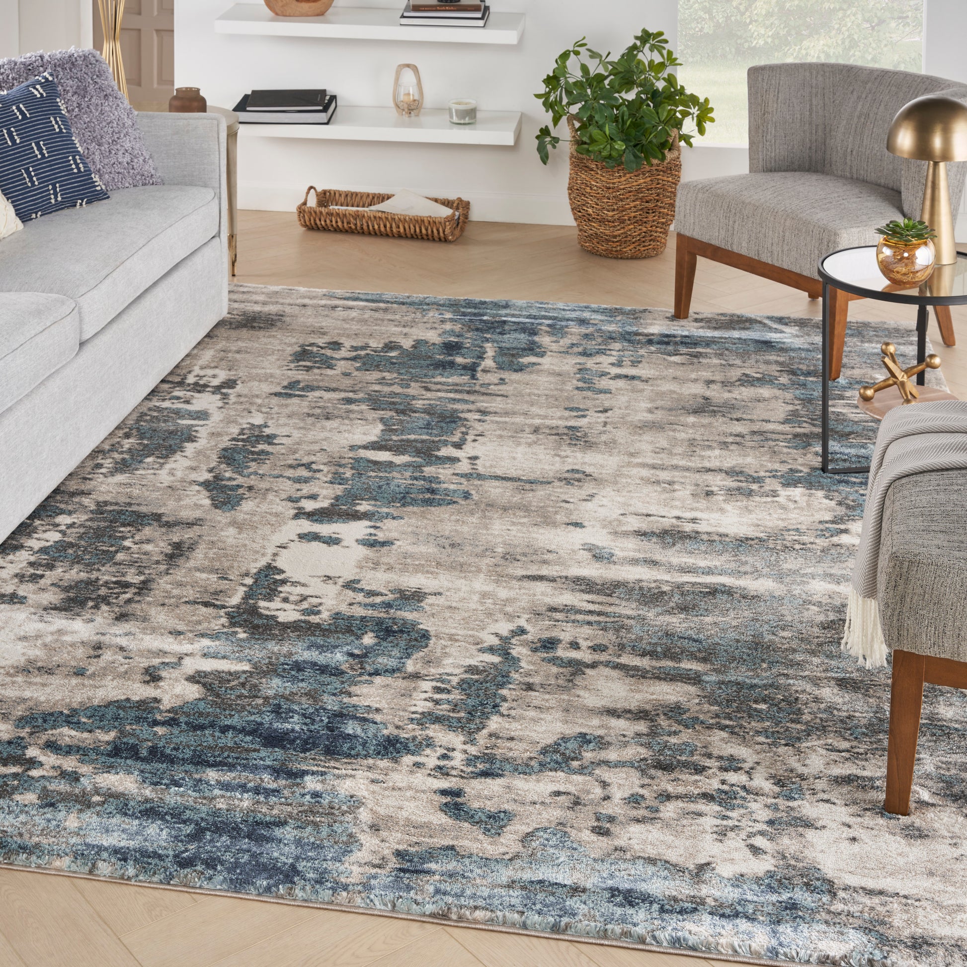 Distressed blue-gray beige abstract area rug in a modern living room with gray sofa, plant, and wooden accents.