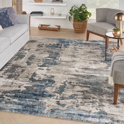 Distressed blue-gray beige abstract area rug in a modern living room with gray sofa, plant, and wooden accents.