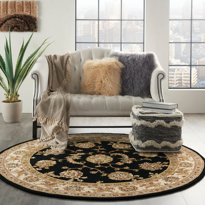 Round black and cream oriental rug with floral border under a white tufted sofa; faux fur pillows and shaggy ottoman.