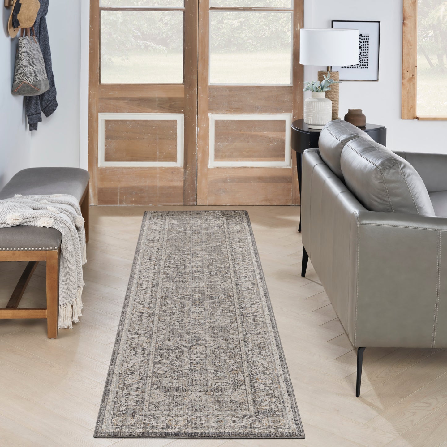 Gray patterned runner rug in a modern living room with a gray leather sofa, wooden doors, and a bench with a throw blanket.