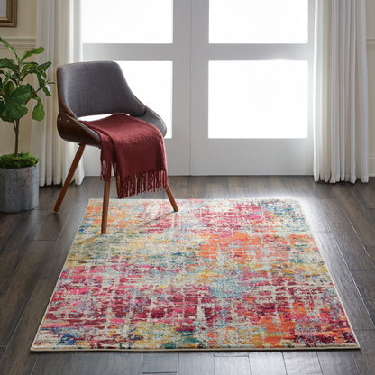 Colorful abstract area rug on dark wood floor beside a mid-century gray upholstered chair with a burgundy throw.