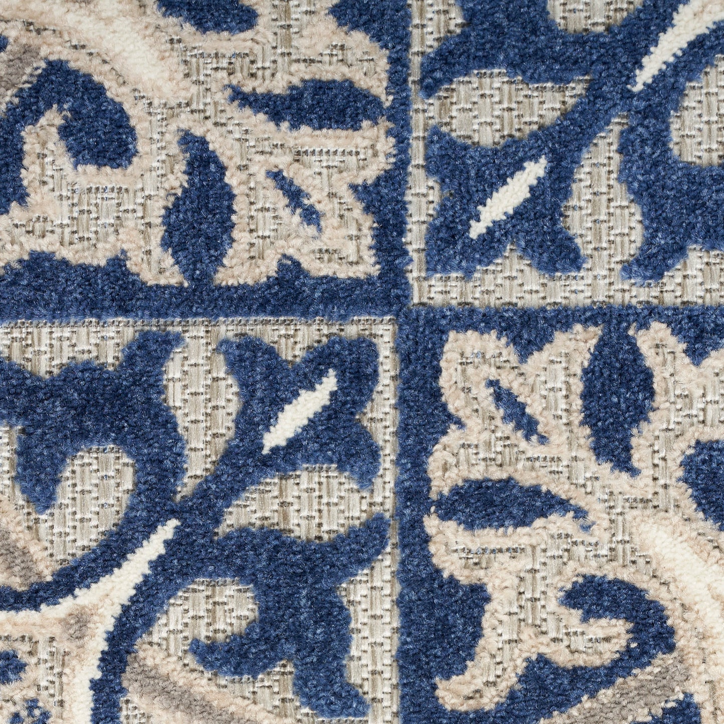 Close-up of a blue and beige damask rug pattern with floral scrolls on a woven background.