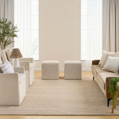 Cream living room with beige sofa, two cube ottomans, woven rug, potted plant, neutral curtains.