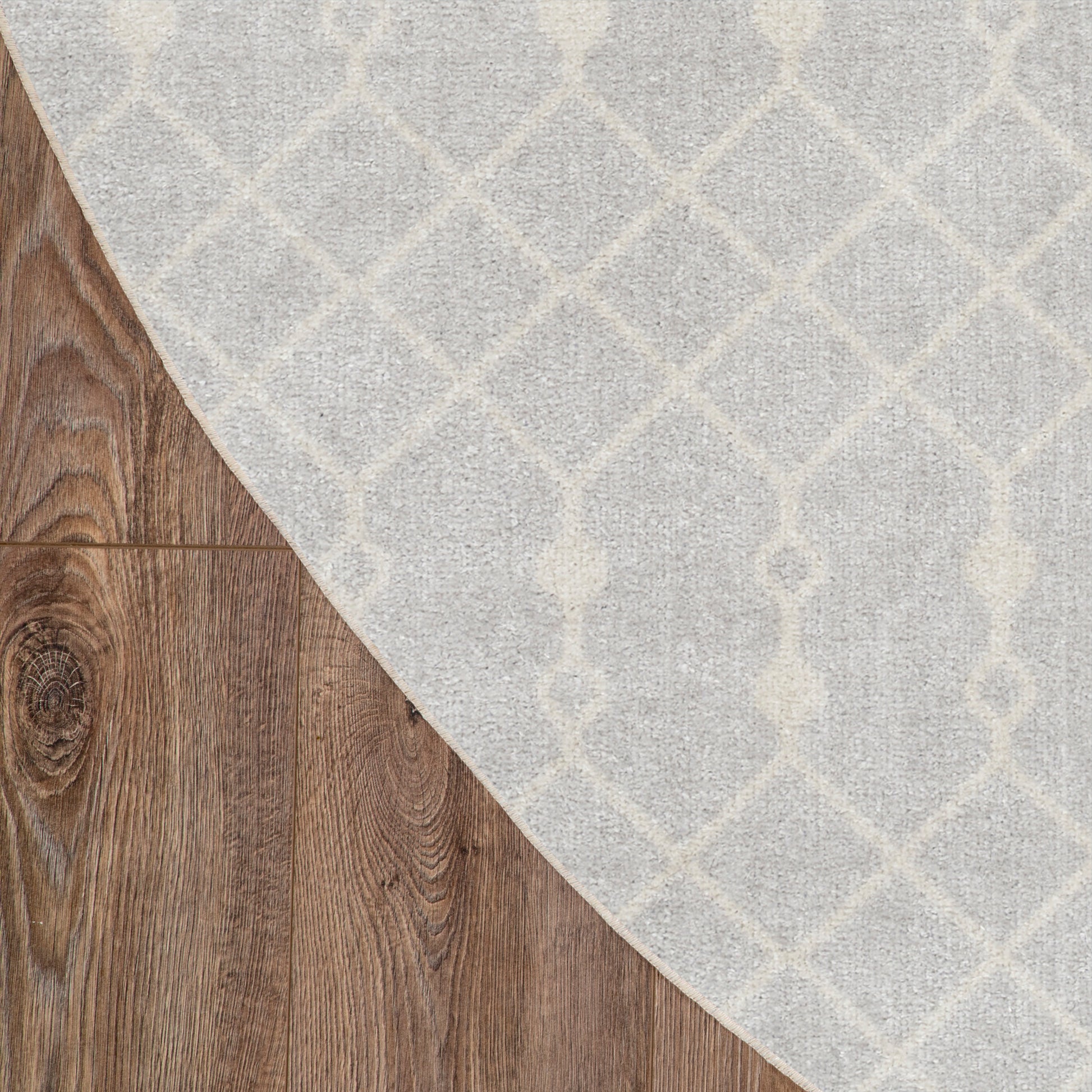 Light gray woven area rug with white geometric trellis pattern and curved edge over brown wood floor.