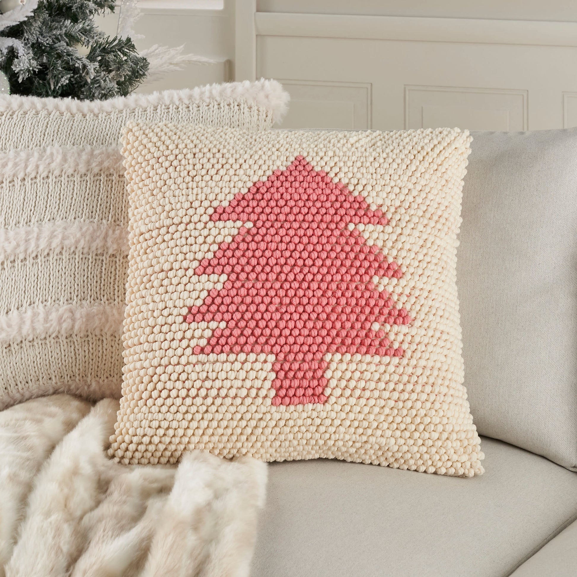 Beige tufted pom-pom pillow with pink Christmas tree motif on a light sofa.