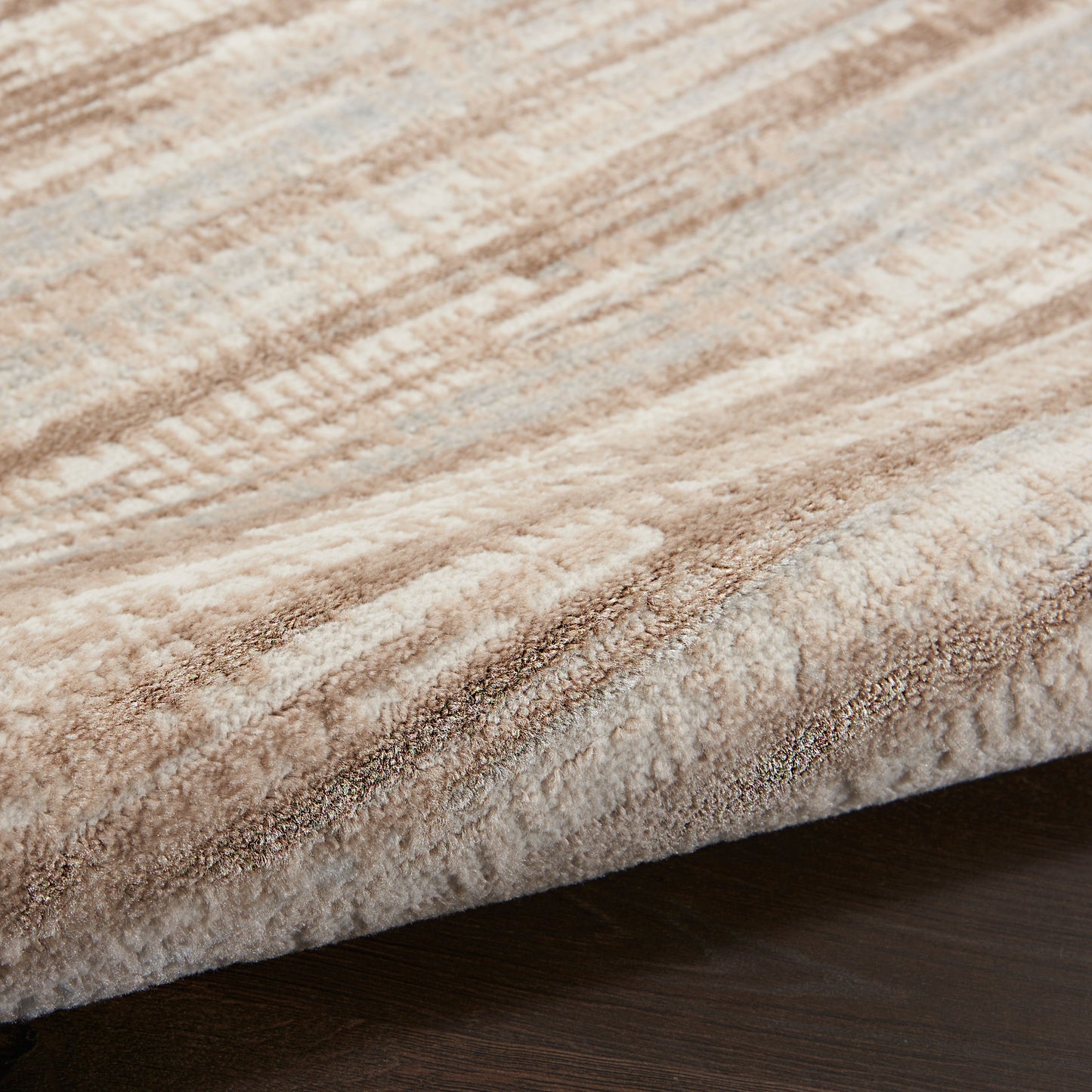 Close-up of a plush beige-tan area rug with abstract stripe pattern resting on dark wood floor.