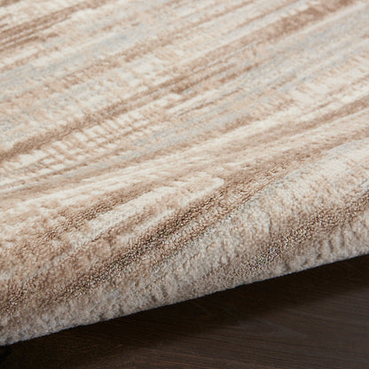 Close-up of a plush beige-tan area rug with abstract stripe pattern resting on dark wood floor.
