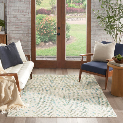 Bright living room with white tufted sofa, beige knit throw, blue chair, wooden side table, and cream chevron rug.