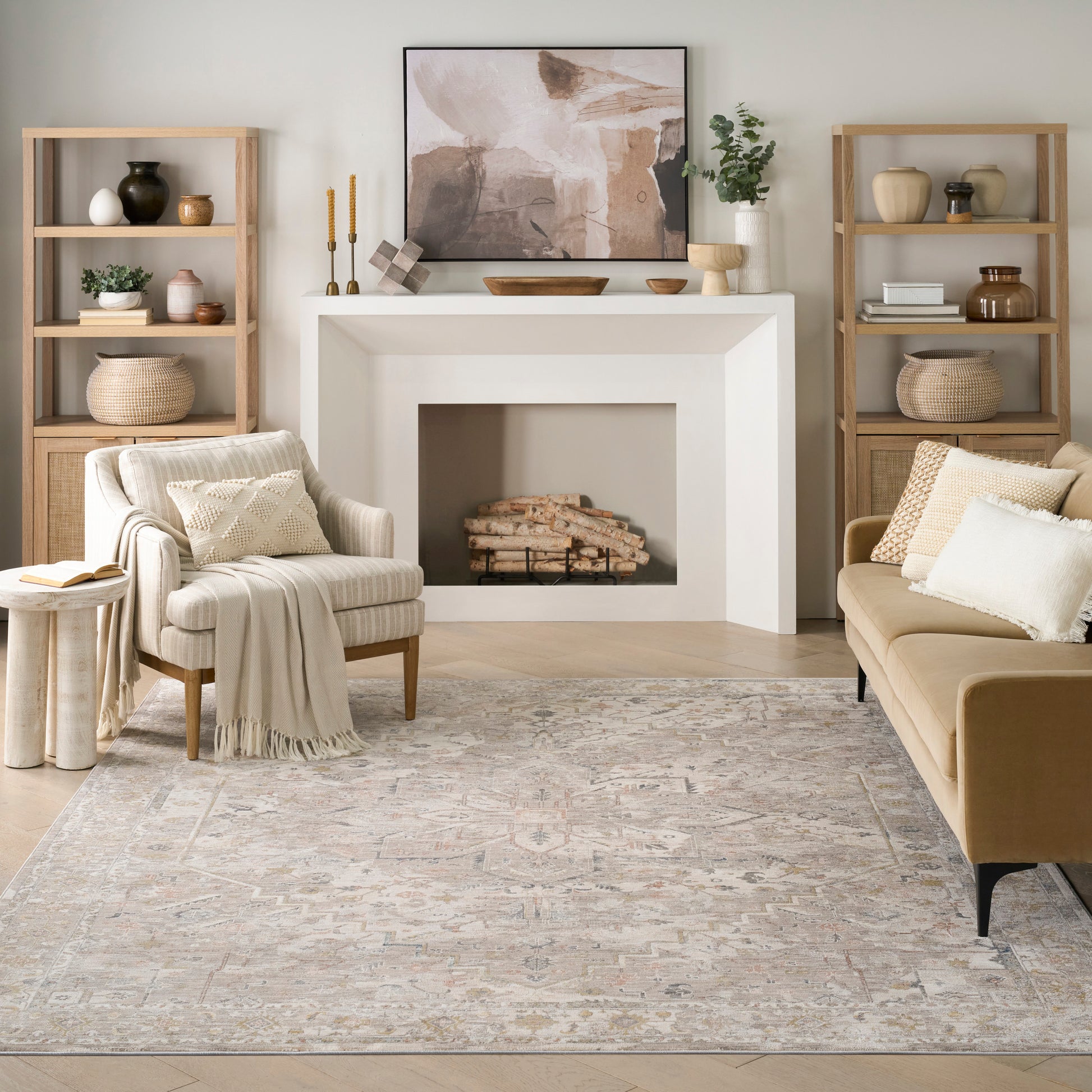 Cozy living room with a white geometric fireplace, light wood shelves, beige sofa and armchair, and a neutral rug.