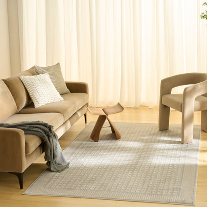 Beige fabric sofa with white textured pillow and gray throw, curved beige chair, wooden stool, light gray patterned rug.