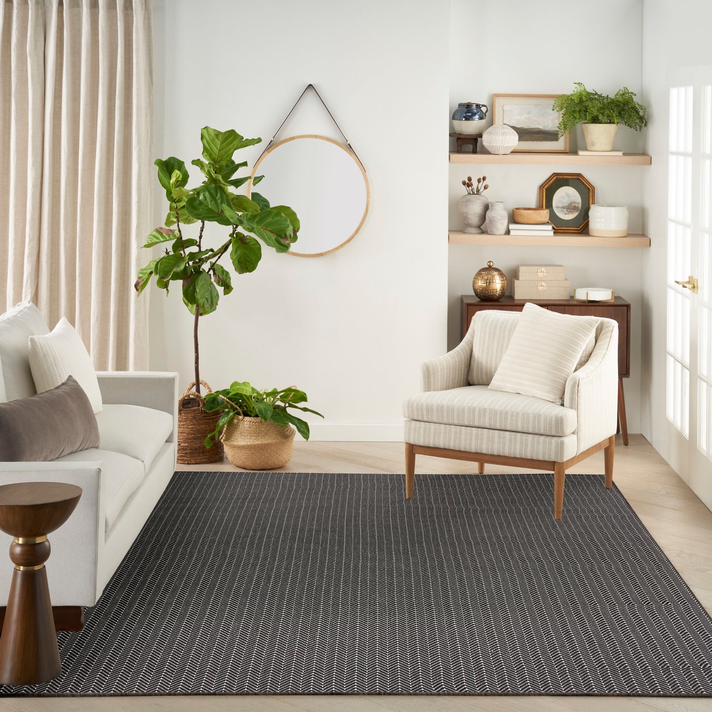 Neutral living room with beige striped armchair, light sofa, dark striped rug, potted plants, and wooden shelves.