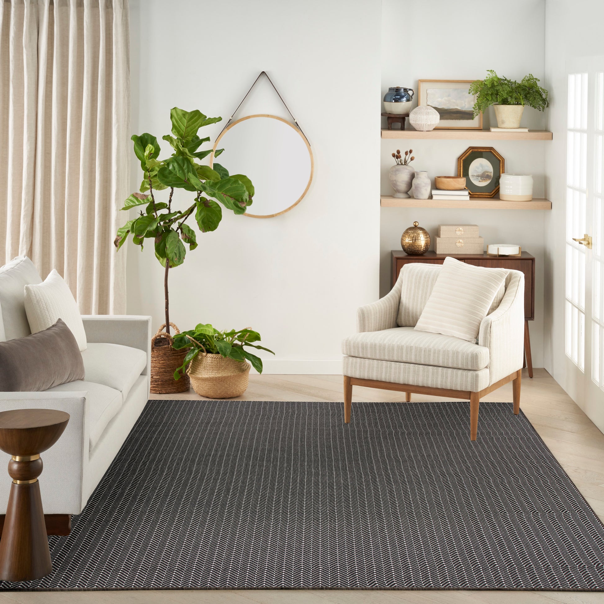Neutral living room with beige striped armchair, light sofa, dark striped rug, potted plants, and wooden shelves.