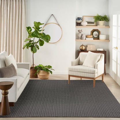 Neutral living room with beige striped armchair, light sofa, dark striped rug, potted plants, and wooden shelves.