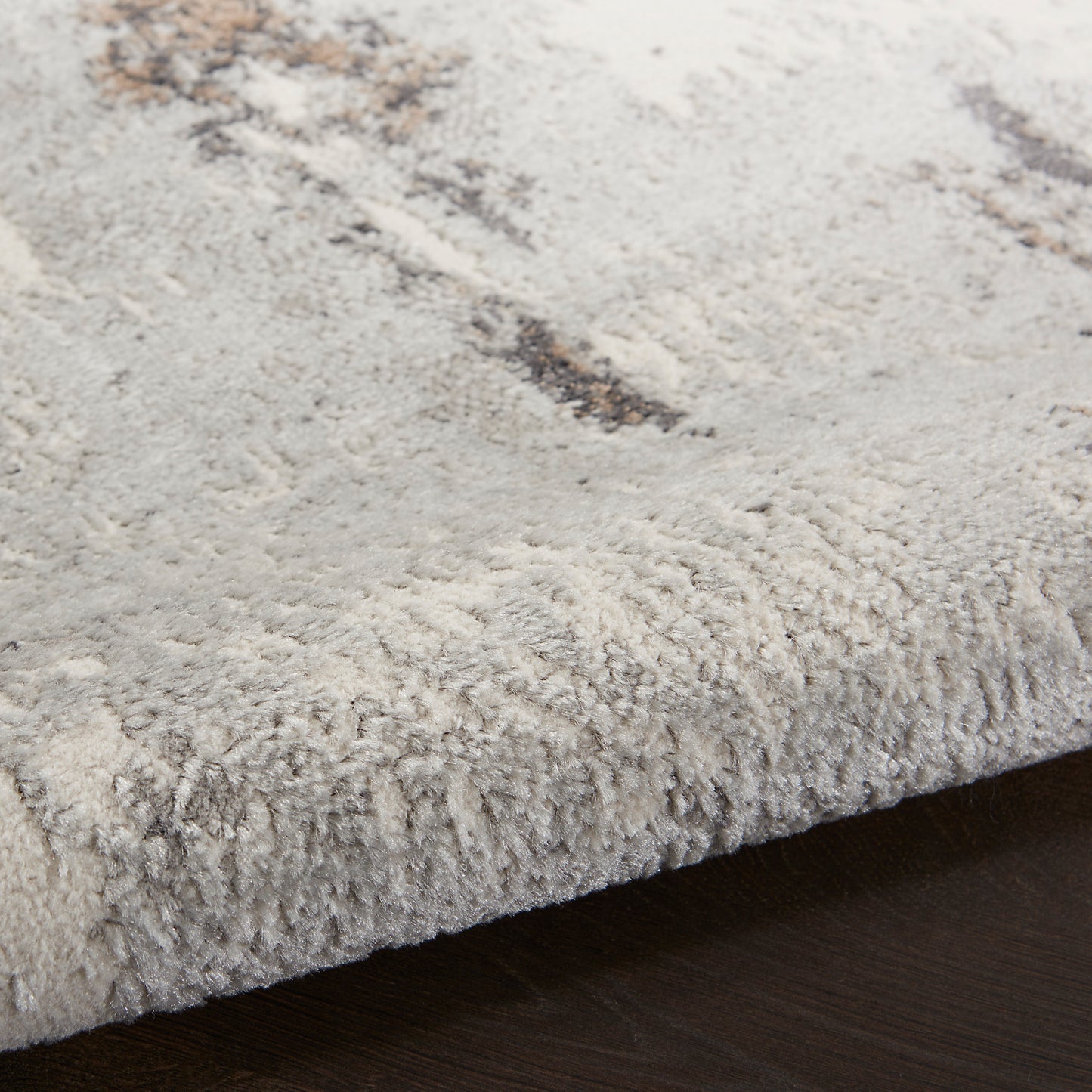 Close-up of a plush light-gray shag rug with beige-brown abstract pattern, edge on dark wood floor.