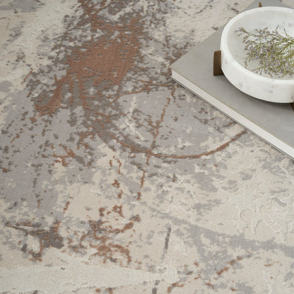Abstract beige, gray and brown rug with marbled pattern; white marble bowl and gray hardcover book.