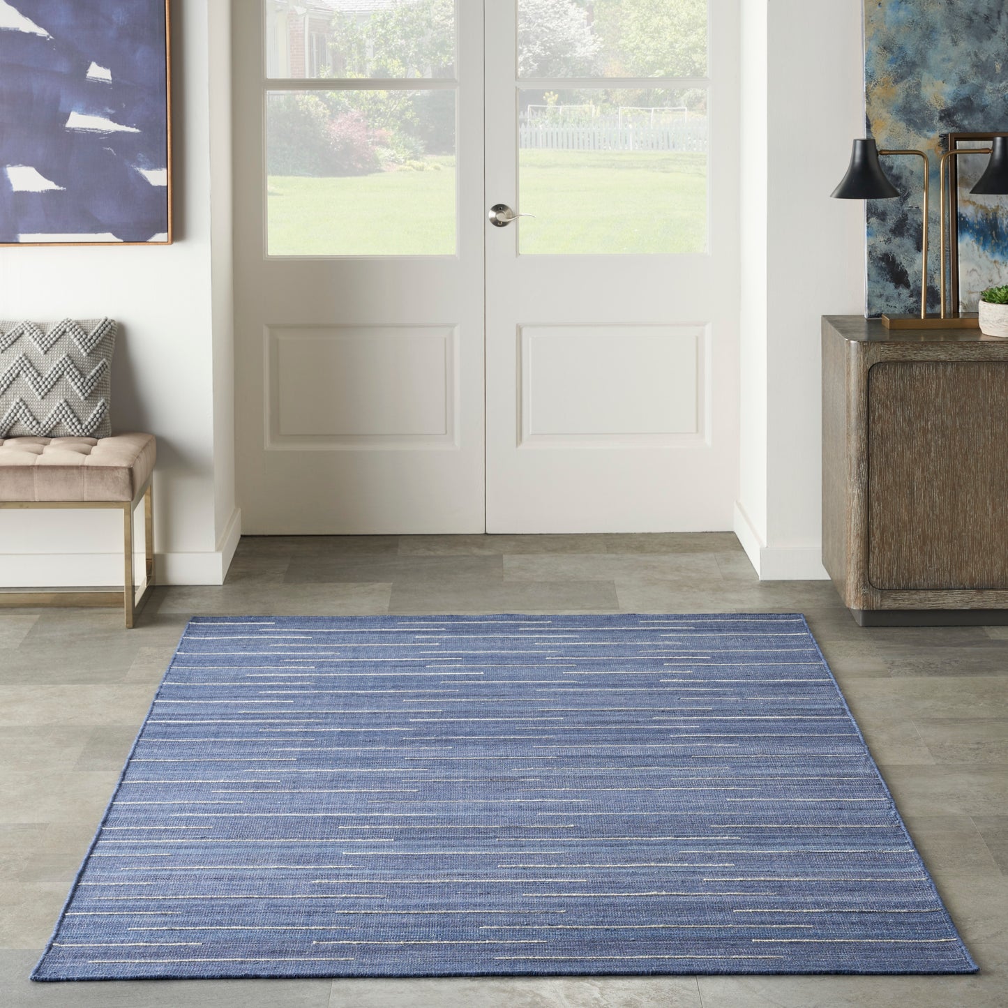 Blue striped rectangular area rug in a bright entryway before white double doors; modern decor with bench and console.