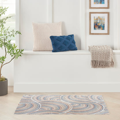 Beige knitted cushion and blue diamond pillow on a white window seat, with beige fringed throw and wavy blue-tan rug.