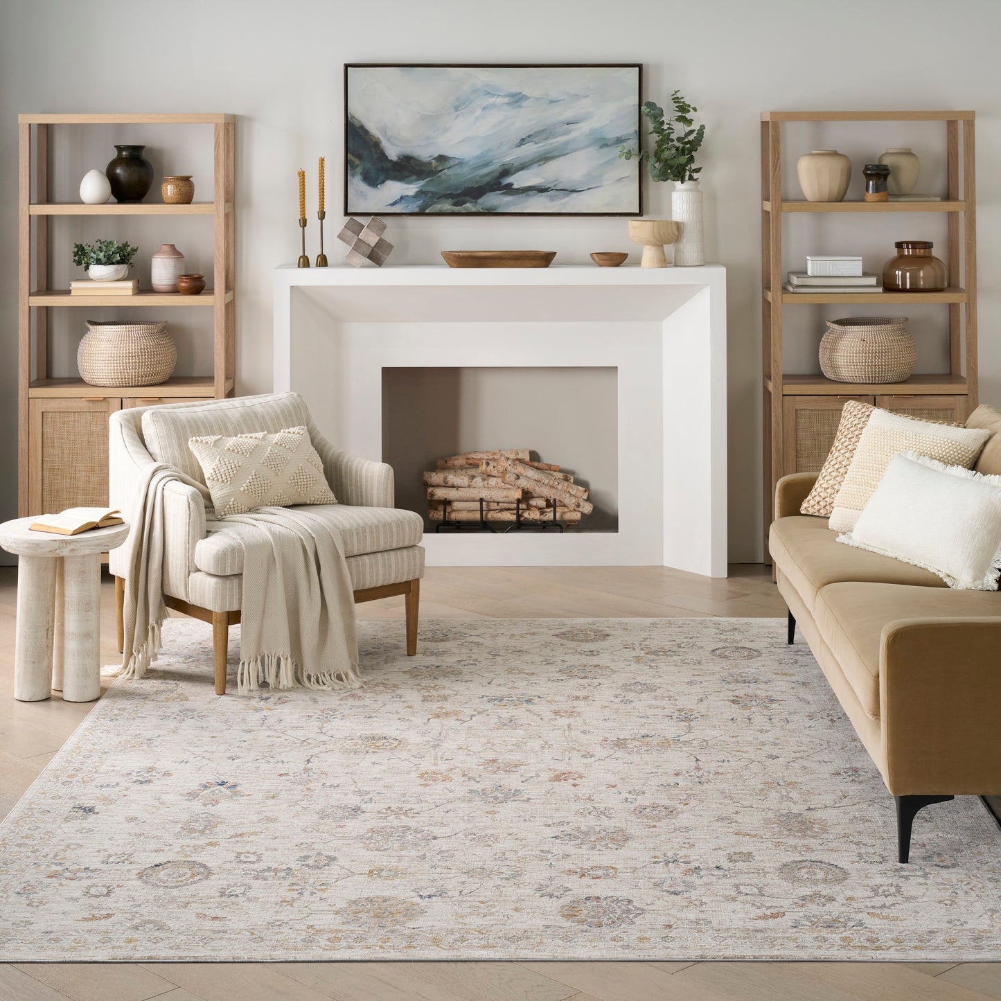 Neutral living room with white angular fireplace, beige sofa, cream armchair, light wood shelves, patterned rug.