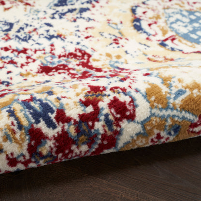 Thick plush area rug with cream base and red, blue, and gold floral pattern, edge resting on dark wood floor.