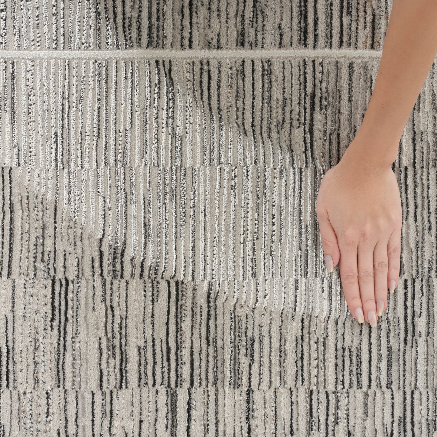 Beige & gray striped textured rug with vertical lines; a hand rests on the plush woven surface.