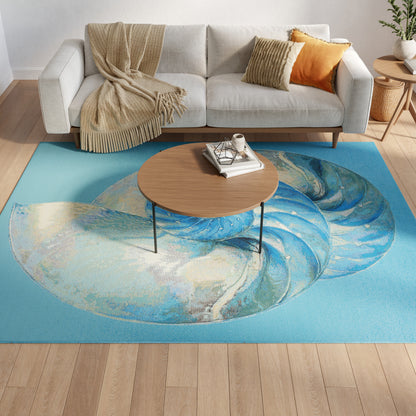 Light gray sofa with beige fringed throw and orange cushion, round wood coffee table on a blue swirl rug.