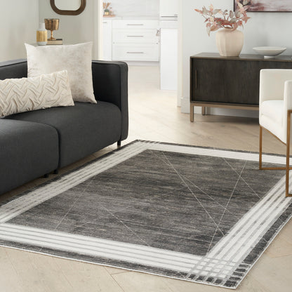 Dark gray area rug with a light striped border in a modern living room; charcoal sofa and cream cushions.