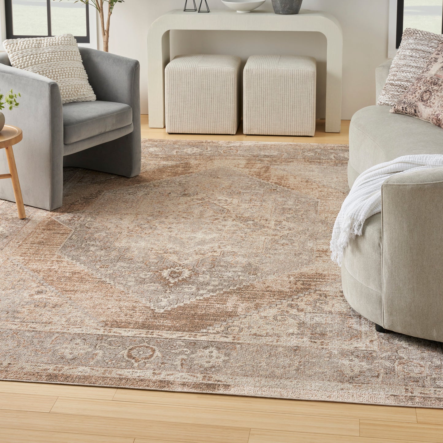 Neutral living room with beige rug, gray fabric armchair, beige sofa, cream curved console, and two cream ottomans.