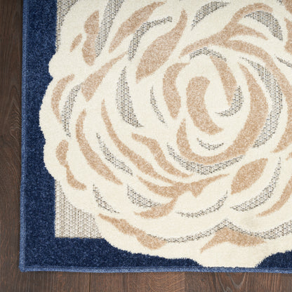 Tufted area rug with beige rose-like floral motif on ivory center and dark navy border, on a wood floor.
