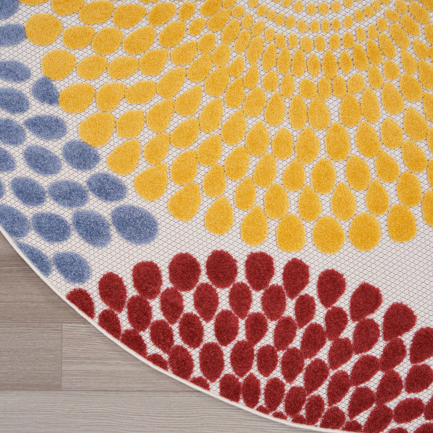 Round rug with yellow, red, and blue teardrop-shaped dots against a white backdrop; bold, modern dotted arc pattern.