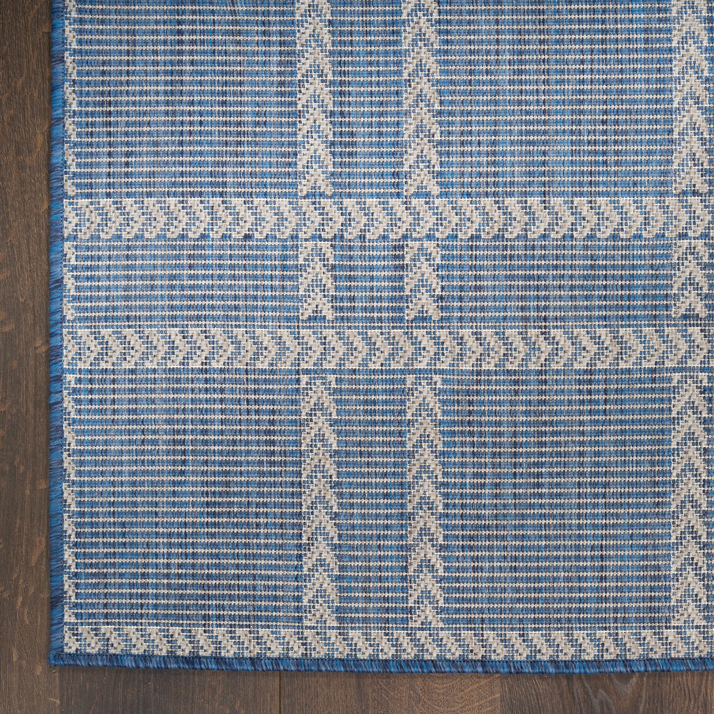 Blue woven rug with white geometric ladder and zigzag motifs and border, on a dark wooden floor.