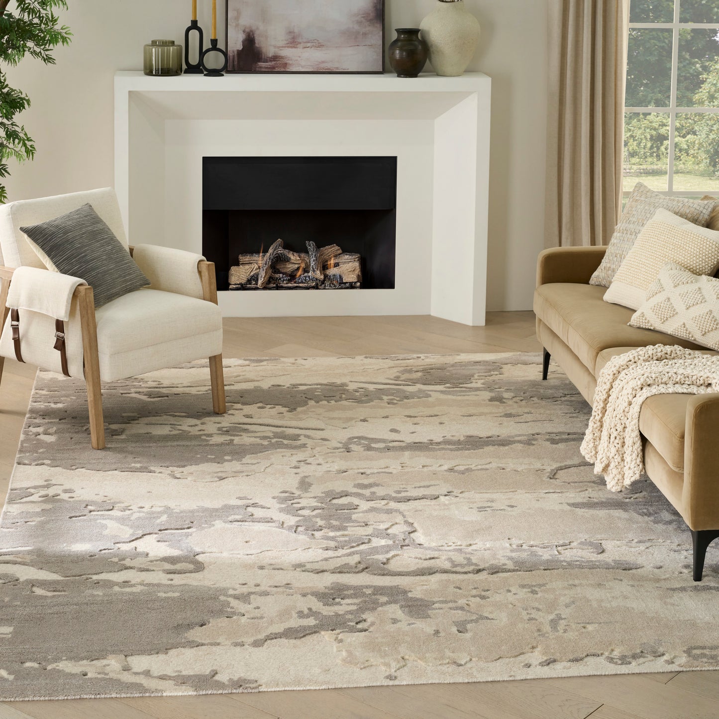 Neutral living room with white modern fireplace, beige sofa, light armchair, textured gray rug, logs in black hearth.